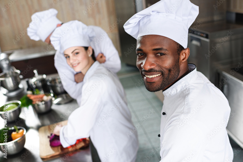 Multiracial chefs team smiling while cooking by kitchen counter