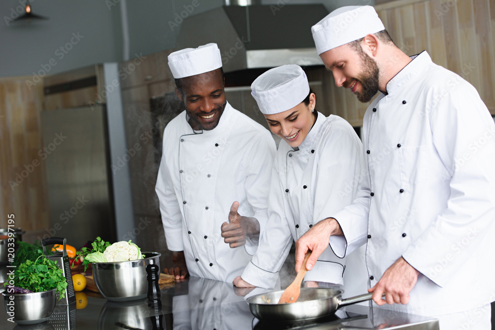 multicultural chefs frying vegetables on frying pan at restaurant kitchen multicultural chefs frying vegetables on frying pan at restaurant kitchen