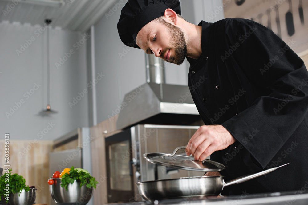 side view of handsome chef cooking with frying pan at restaurant kitchen side view of handsome chef cooking with frying pan at restaurant kitchen