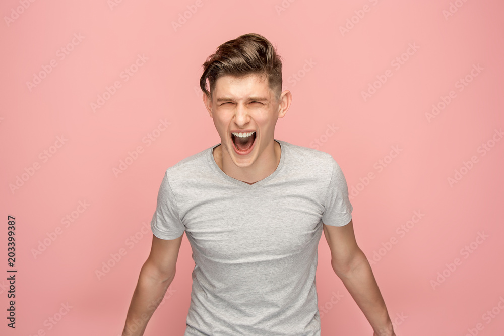 The young emotional angry man screaming on pink studio background The young emotional angry man screaming on pink studio background