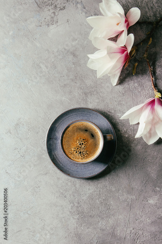 Blue cup of black espresso coffee and spring flowers magnolia branches over grey texture background. Top view, space. Spring greeting card,