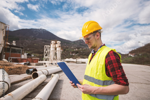 Construction worker in helmet, high visability vest writing on clipboard photo