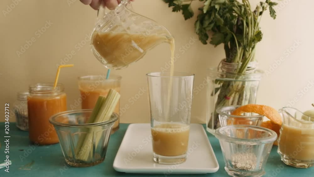 Pouring smoothies in a tall glass, carrots banana, celery and orange smoothie, healthy lifestyle, ingredients on a table behind and yellow background . Pouring smoothies in a tall glass, carrots banana, celery and orange smoothie, healthy lifestyle, ingredients on a table behind and yellow background .