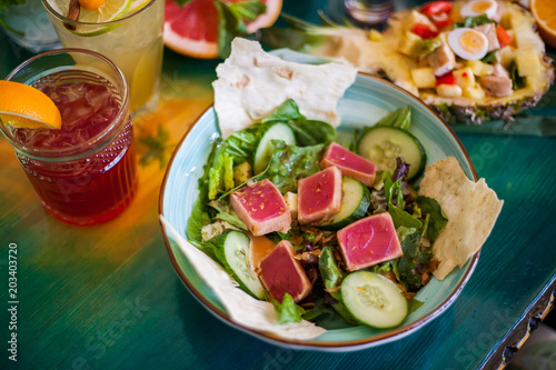 Salads from fresh products with meat, fish, chicken and vegetables on the table among colorful refreshing cocktails with ice.