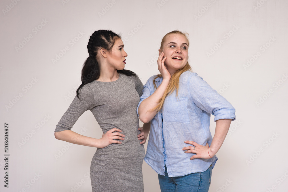 Portraits on the gray background of two girls girlfriends showing emotions. Portraits on the gray background of two girls girlfriends showing emotions.