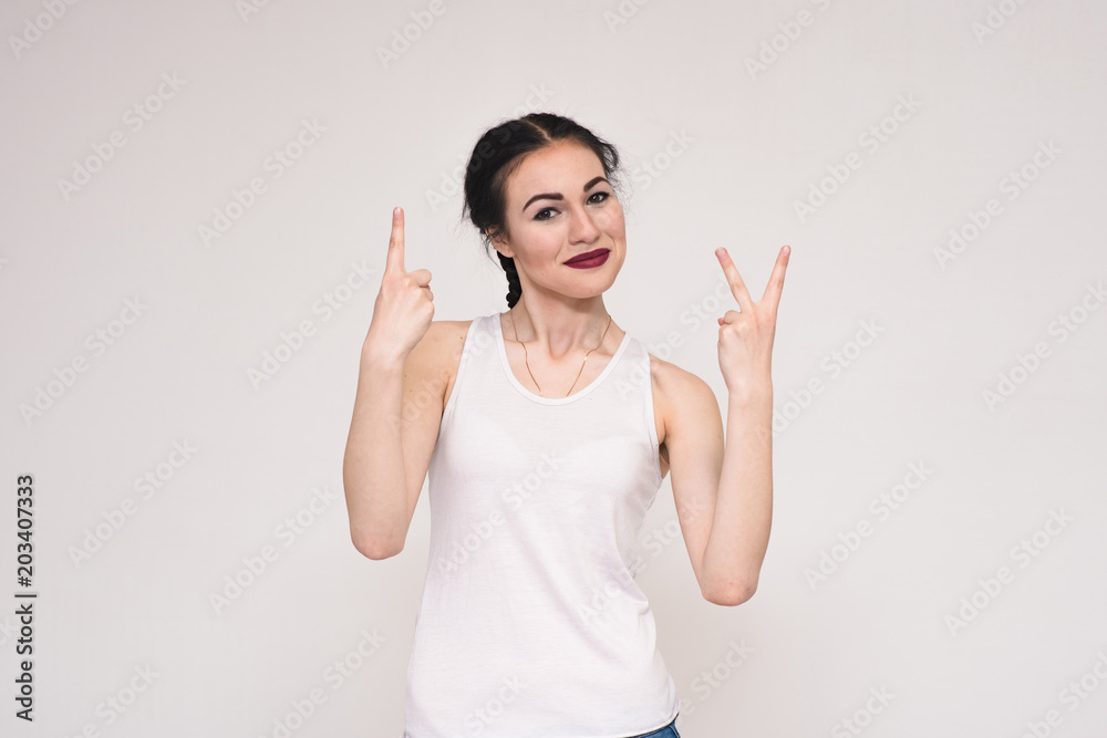 portrait of a beautiful brunette girl in a T-shirt on a gray background showing the fingers portrait of a beautiful brunette girl in a T-shirt on a gray background showing the fingers