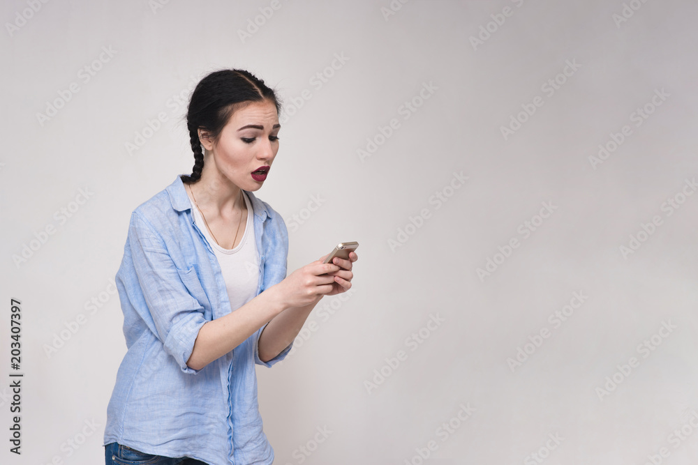 Portrait of a beautiful brunette girl in a shirt on a gray background with a smartphone. Portrait of a beautiful brunette girl in a shirt on a gray background with a smartphone.
