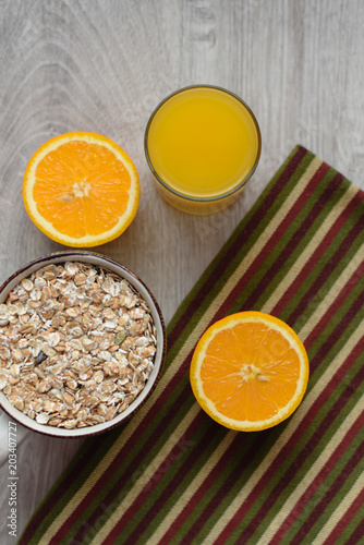 Still life healthy breakfast of muesli, oranges and orange juice in a glass, striped napkin on a wooden background.