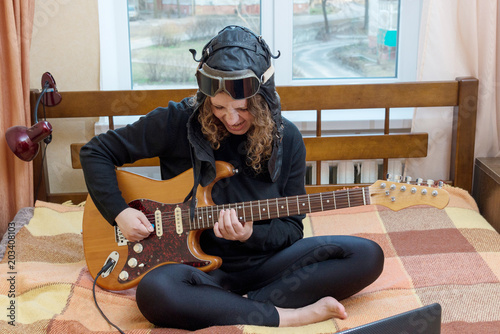 Girl playing electric guitar sitting on the bed