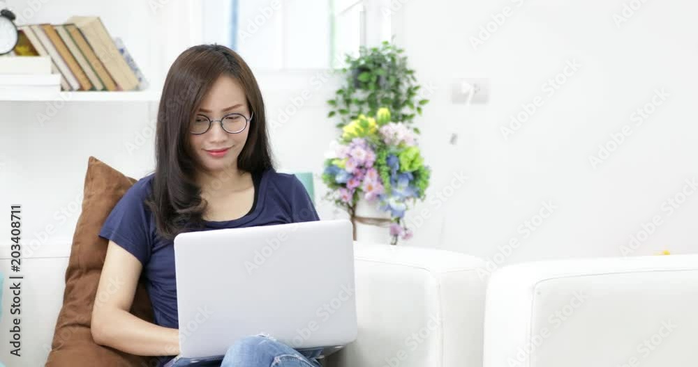 Young woman in glasses sitting on the sofa using laptop at home on living background for working. Indoor. Young woman in glasses sitting on the sofa using laptop at home on living background for working. Indoor.