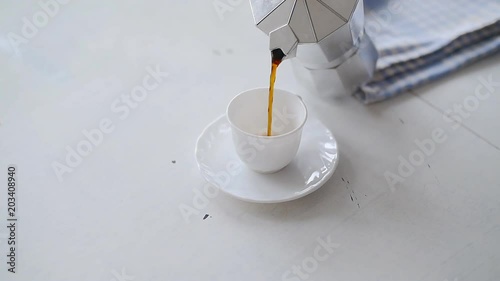 Hand pouring coffee from a Moka Pot. White table photo