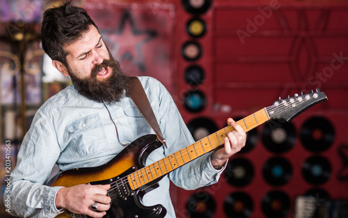 Rock music concept. Talented musician, soloist, singer play guitar in music club on background. Man with shouting face play guitar, singing song, play music. Musician with beard play electric guitar.