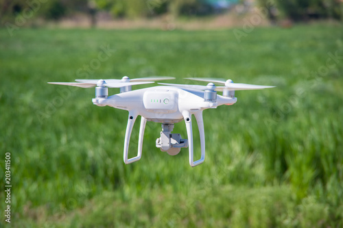 The modern drone, quadrocopter is in the air against the background of the sky and grass