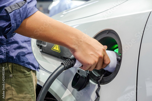 Close-up asia men hands who are fueling a new vehicle electrification via rechargeable electricity machine, Electric cars are a new innovation in the future, built to replace cars powered by oil. photo