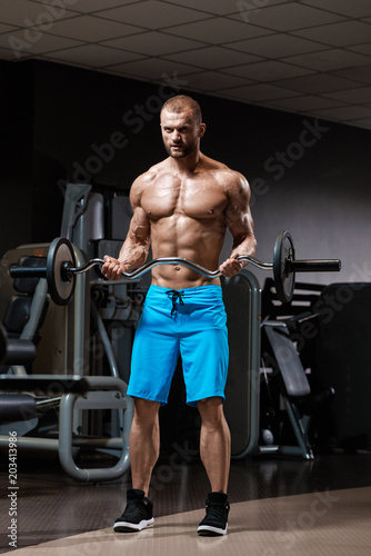 Muscular strong man doing exercises with barbell in gym