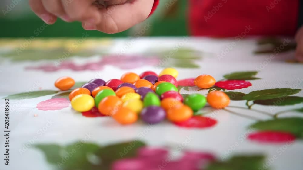 Little colored candy. Child hands takes candy from the table. Hands close up Little colored candy. Child hands takes candy from the table. Hands close up