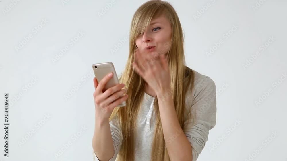 modern youth. beautiful long-haired girl of European appearance with blond hair expressively talking on a video communication smartphone near the white wall modern youth. beautiful long-haired girl of European appearance with blond hair expressively talking on a video communication smartphone near the white wall