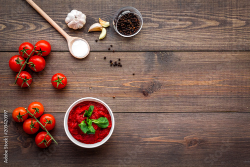 Ingredients for tomato sauce. Cherry tomatoes, garlic, green basil, black pepper, salt in spoon on dark wooden background top view copy space