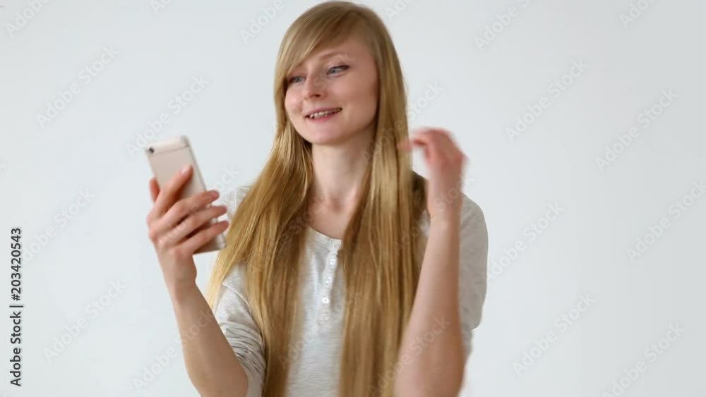 modern youth. beautiful long-haired girl of European appearance with blond hair expressively talking on a video communication smartphone near the white wall modern youth. beautiful long-haired girl of European appearance with blond hair expressively talking on a video communication smartphone near the white wall