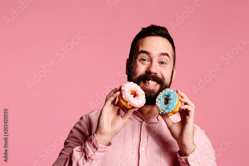 Foto Sweet tooth bliss : Smiling man holding a blue and pink donut, isolated on pink