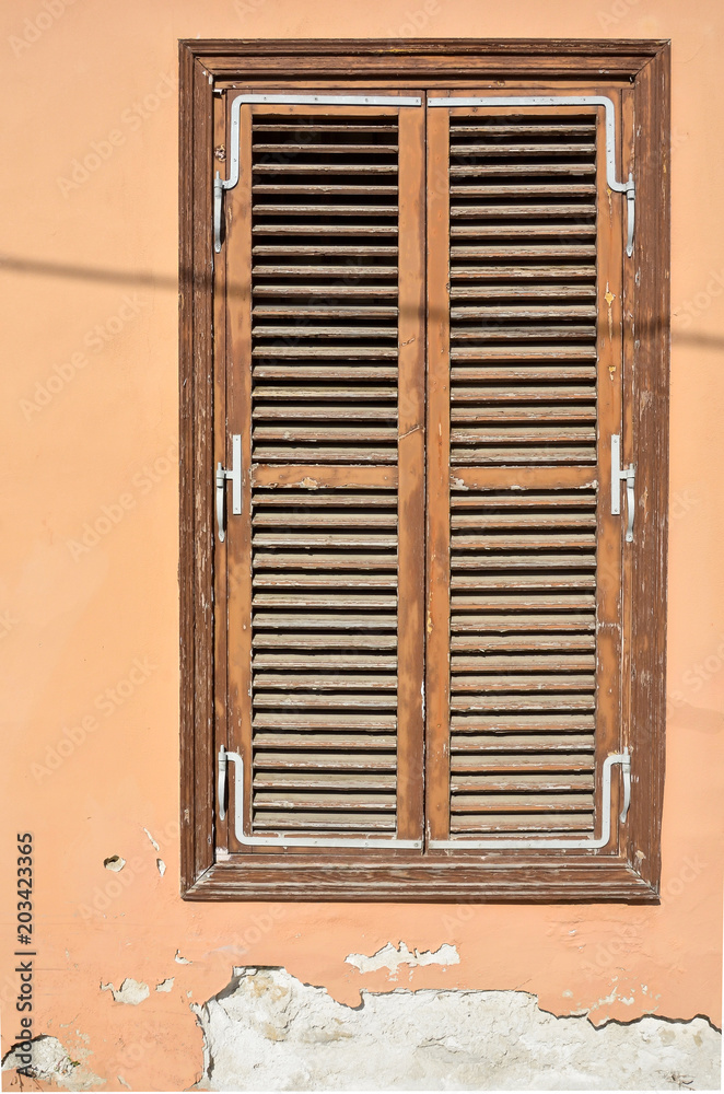 Old brown wooden window with shutters and wall with cracked paint. Vintage background. Cyprus
