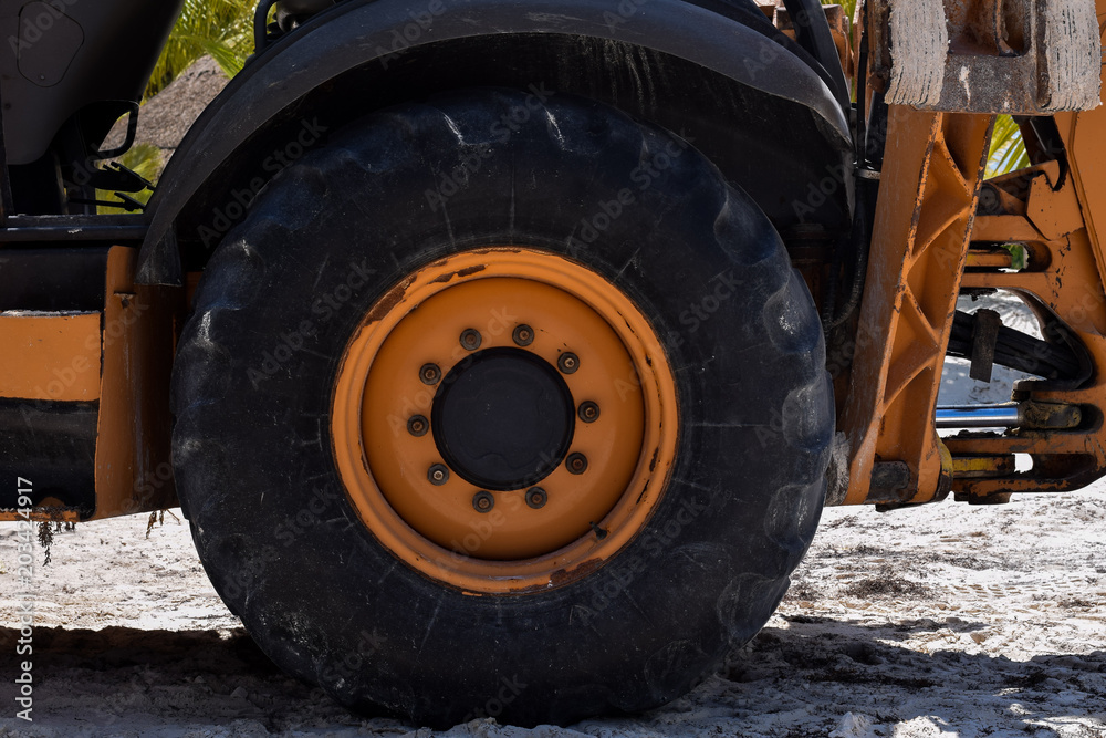 Großes Traktorrad an orangefarbenem Traktor am Strand Großes Traktorrad an orangefarbenem Traktor am Strand