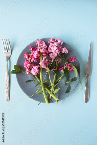 creative layout. Pink flowers on a plate, fork and knife on a blue background. Concept. Flat lay. Place for text
