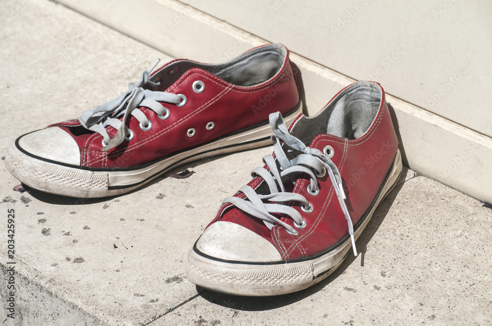 Abandoned heavy used old grunge weathered red sport sneakers on street stone surface Abandoned heavy used old grunge weathered red sport sneakers on street stone surface