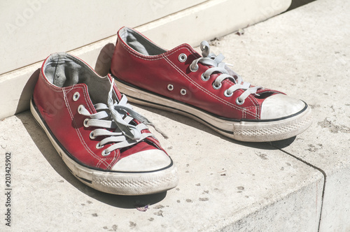 Abandoned heavy used old grunge weathered red sport sneakers on street stone surface