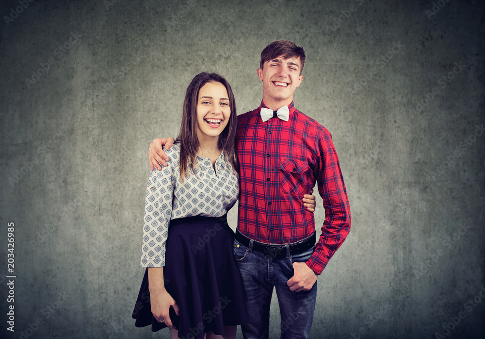 Cheerful young woman and man embracing one another, looking and smiling at camera