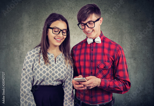 Happy eccentic hipster guy holding smart phone, showing his girlfriend funny pictures photo