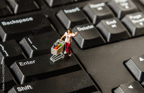 tiny miniature figurine woman with shopping cart on computer keyboard. ecommerce shopping concept.