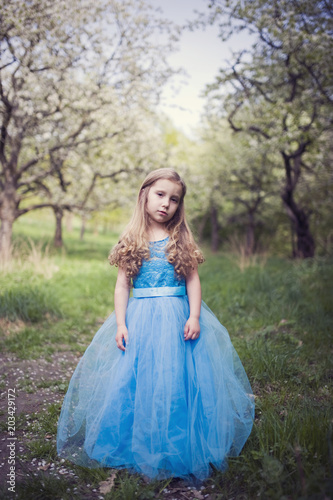 Beautiful little princess gril with blue dress in spring orchard