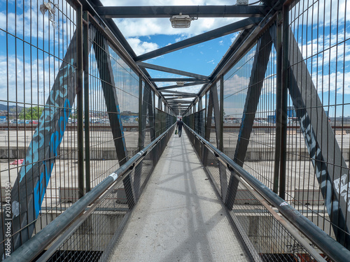 Hombre camina a traves de un puente de metal. 