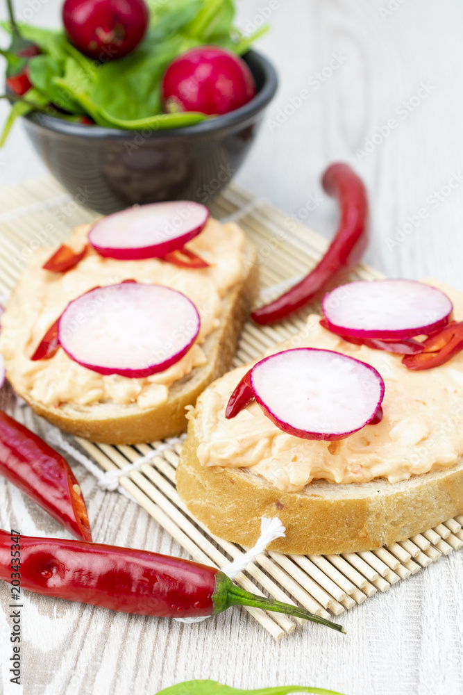 Bread with a spicy cheese spread, pieces of peppers, slices of radish and baby spinach. Healthy and spicy breakfast concept. Bread with a spicy cheese spread, pieces of peppers, slices of radish and baby spinach. Healthy and spicy breakfast concept.