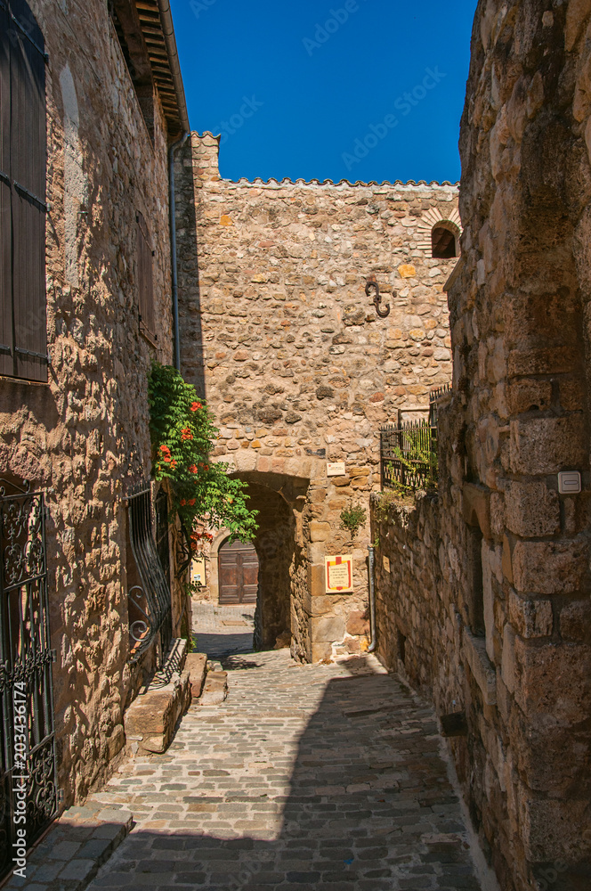 View of stone houses in a narrow alley under blue sky, at the gorgeous medieval hamlet of Les Arcs-sur-Argens, near Draguignan. Located in the Provence region, Var department, southeastern France View of stone houses in a narrow alley under blue sky, at the gorgeous medieval hamlet of Les Arcs-sur-Argens, near Draguignan. Located in the Provence region, Var department, southeastern France