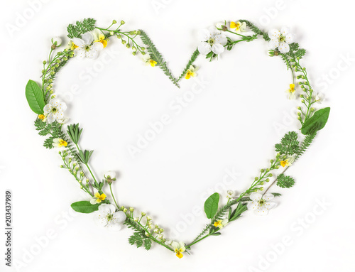 Heart symbol made of spring flowers and leaves isolated on white background. Flat lay. Top view.
