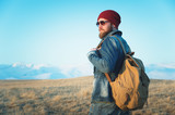 Portrait of a thoughtful stylish hipster with a beard in sunglasses and a hat with a backpack on the background of the snow-capped Mount Elbrus in the Caucasus at sunset