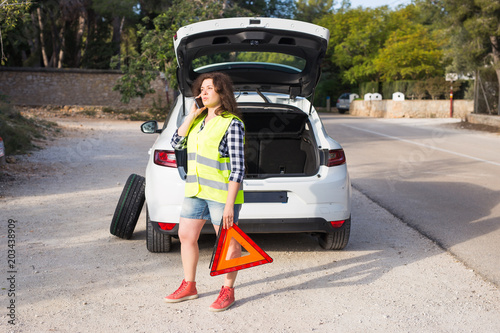 Broken down car with warning triangle. Woman standing alongside her broken down car on the road and making call while waiting for emergancy assistance photo