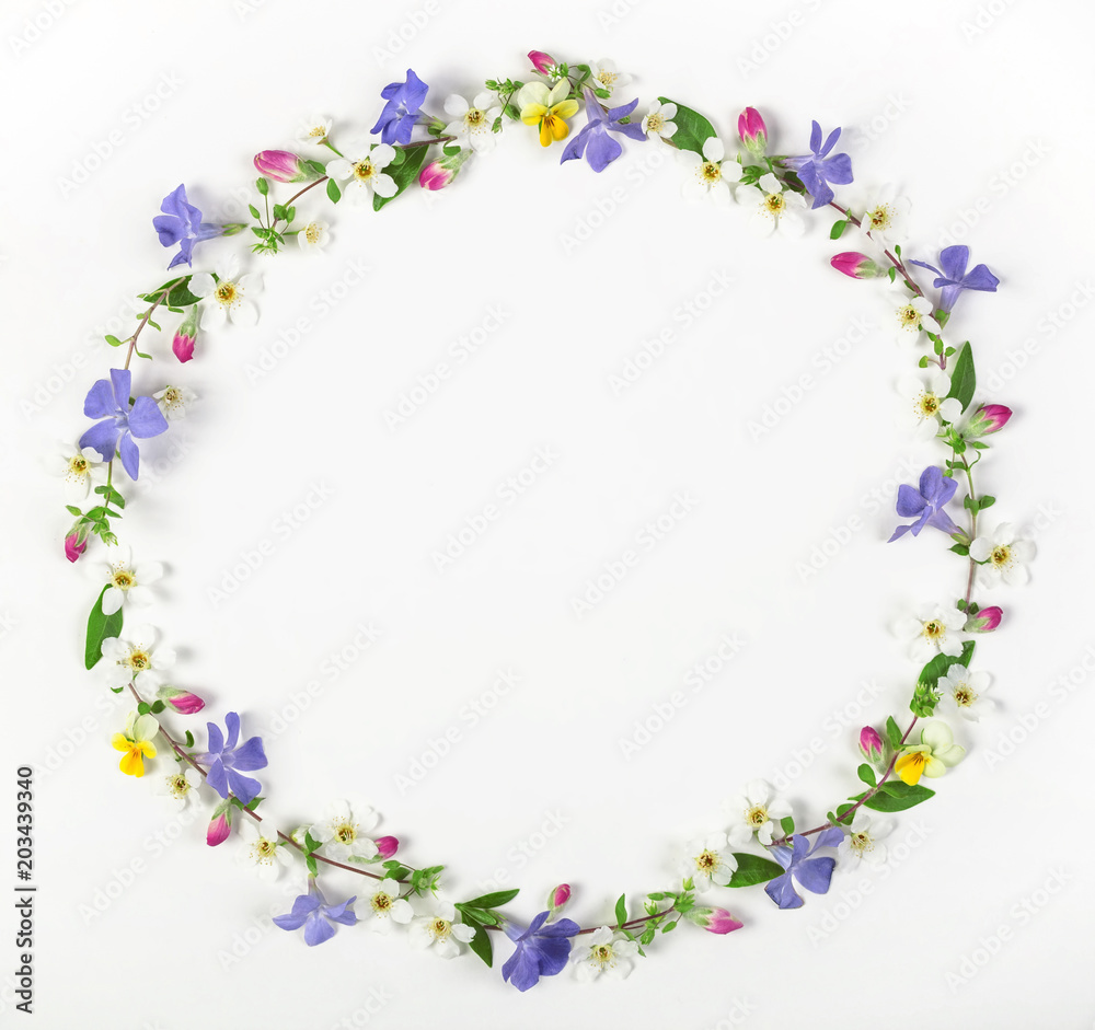 Round frame wreath made of spring wildflowers, lilac flowers, pink buds and leaves isolated on white background. Top view. Flat lay.