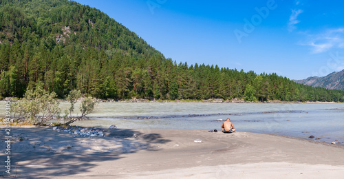 Tourist rests on the sandy river bank in the mountains