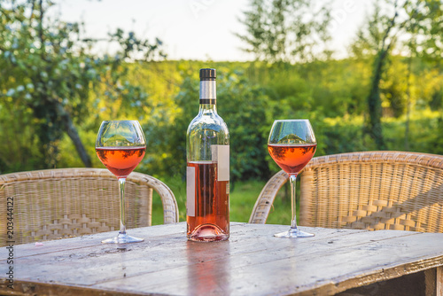 French art of living: bottle of rosé and two glasses of pink wine on a wooden table outdoors