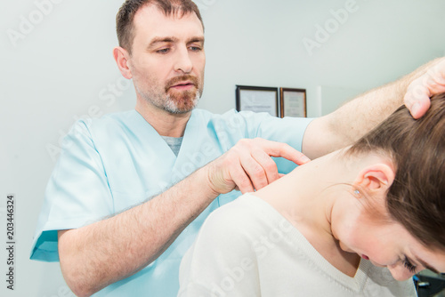 Male neurologist doctor examines cervical vertebrae of female patient spinal column in medical clinic. Neurological physical examination. Osteopathy, chiropractic, physiotherapy. Selective focus.