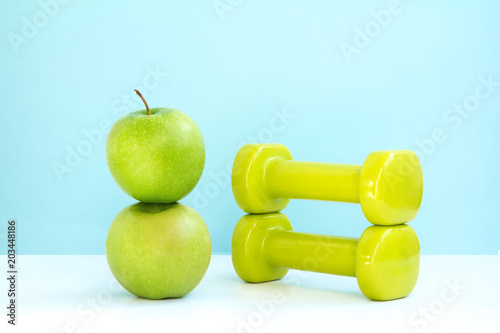 two green apples and dumbbells on blue background