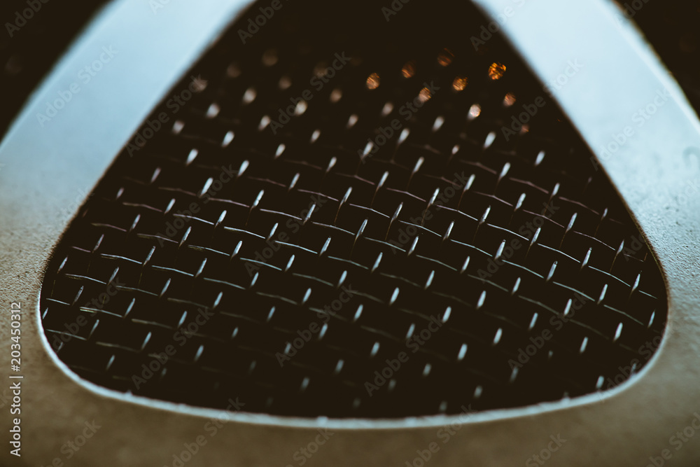 Auto part with shiny mesh. Metallic texture of grid close-up. Triangular shape of grid with gold reflex. Auto part with shiny mesh. Metallic texture of grid close-up. Triangular shape of grid with gold reflex.