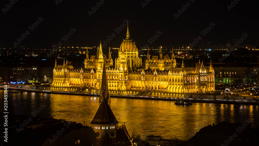 Golden Parliament of Budapest at night with river Danube seen from opposite river bank