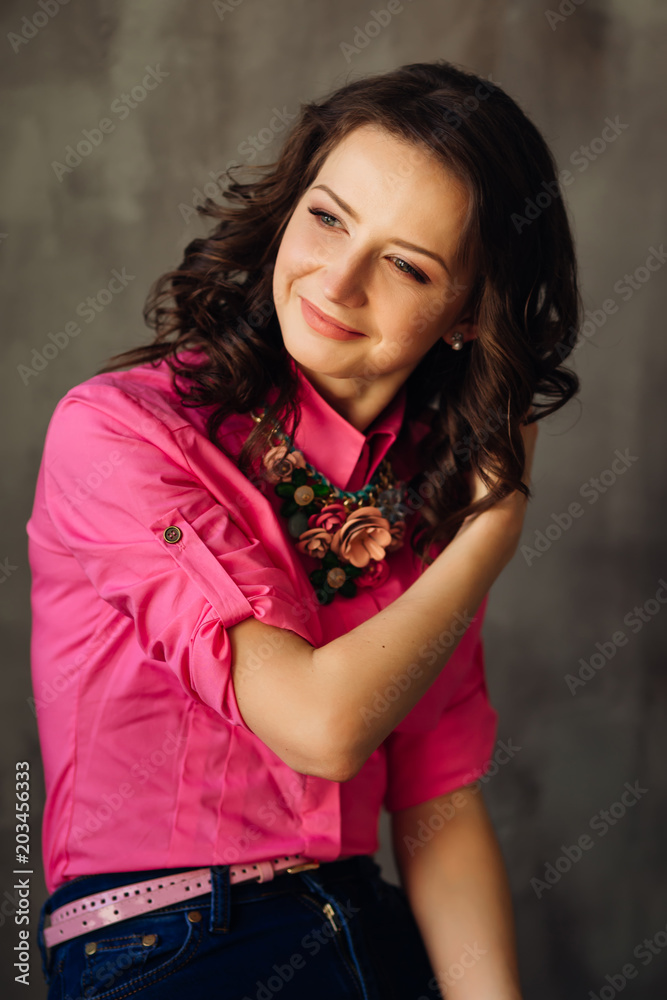 beautiful woman in a pink shirt sitting in a chair on a background of gray wall beautiful woman in a pink shirt sitting in a chair on a background of gray wall