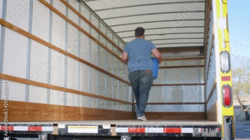 Man loads a moving truck with a blue plastic box in 4k. The young man walks up the metal ramp with a bin of belongings preparing to relocate to a new city. Candid shot represents relocating for work. photo