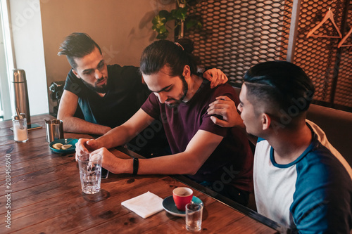 Supportive young men encourage their brokenhearted friend. Arabian guys cheer him up in restaurant. Friendship concept. photo