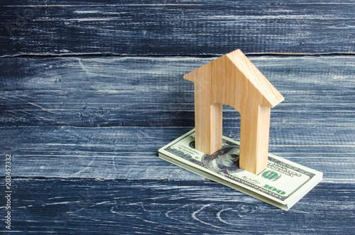 A wooden house stands on a stack of dolor banknotes. The concept of buying and selling immovability, rent of apartments. Credit and mortgage, affordable housing. Utilities payments. photo